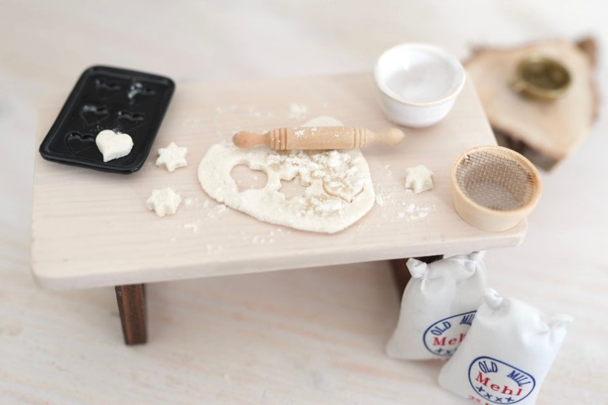 Tisch mit ausgerolltem Keksteig, Backblech, Nudelholz, unfertigen Plätzchen